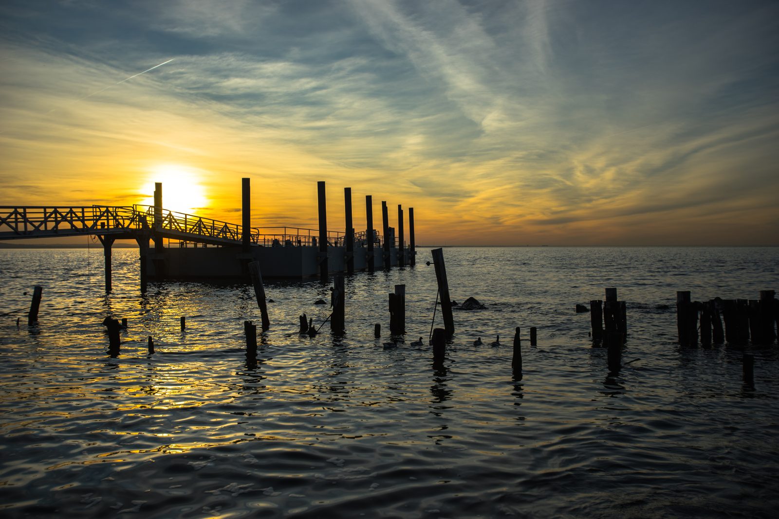 Silhouette of a pier and old wooden pilings in the water at sunset