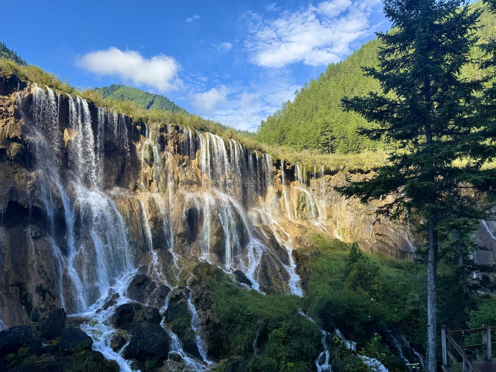 A wide waterfall cascading over a mossy limestone cliff under a blue sky