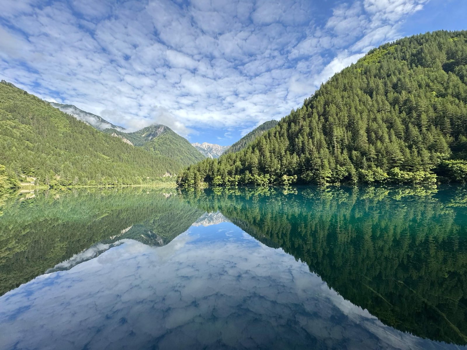 Forested mountains and clouds mirrored in a still turquoise lake